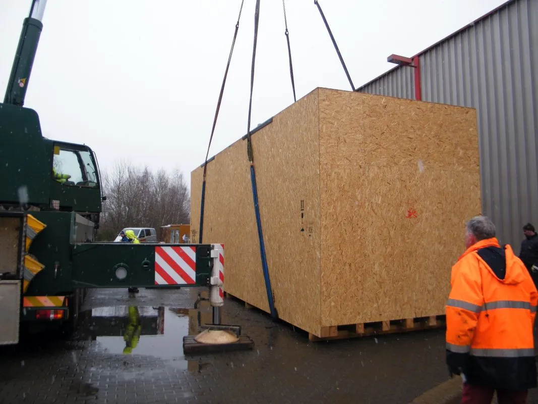 Kran hebt eine große Exportkiste von TVR auf einen Lkw